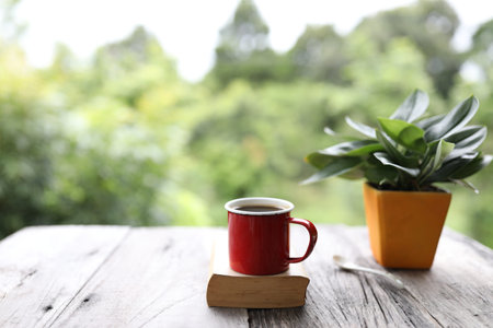Red coffee mug on top of old book with plant pot on rustic wooden tableの写真素材
