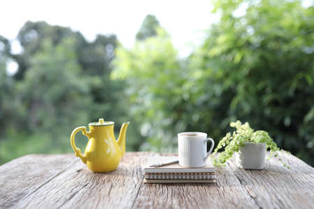 White mug and yellow tea pot and notebook and plant on brown wooden tableの写真素材