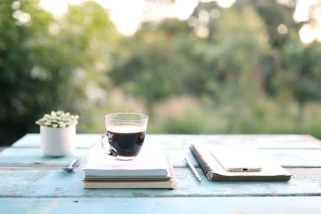 Black coffee cup and thick book and phone and cactus on table at outdoor