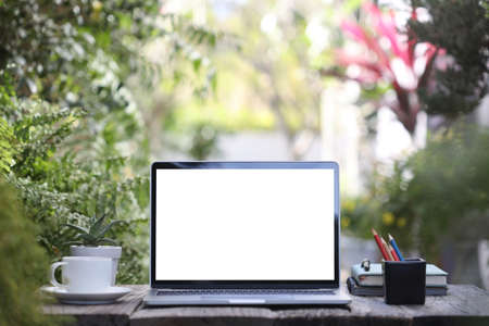 Laptop blank white screen with coffee cup and notebooks on wooden desk at outsideの写真素材