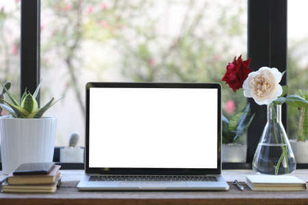 Laptop white blank screen with notebooks and rose vase on wooden tableの写真素材