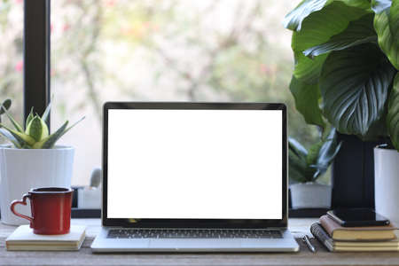 laptop mock up white blank screen with phone and coffee cup and plant pot on wooden tableの写真素材