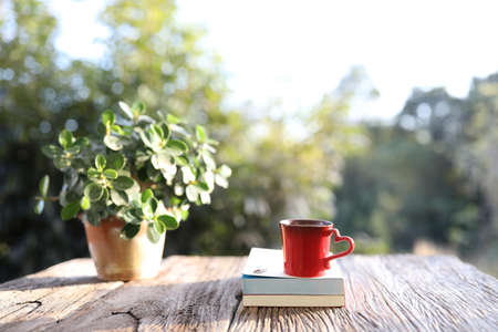Red cup with heart shape handle and notebooks and plant pot on brown wooden table front viewの写真素材