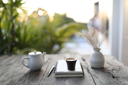 small black tea cup and white kettle and dry flower vase and notebook on wooden tableの写真素材