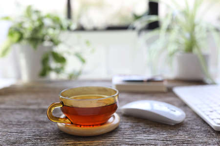 Tea in transparent glass cup on wooden table with mouse and keyboardの写真素材