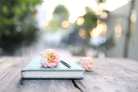 soft pink roses and notebook and pencil on wooden tableの写真素材