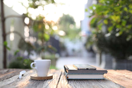 White coffee cup with phone and notebook on wooden table at outdoorの写真素材