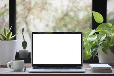 White screen laptop and coffee cup with notebook and plants pot on wooden table work from home