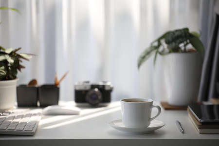 White coffee cup on and mouse keyboard with camera and plant pot on white wooden tableの写真素材