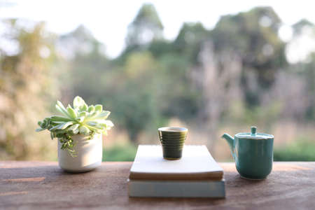 Notebooks and tea cup and blue teapot with plant pot on brown wooden tableの写真素材
