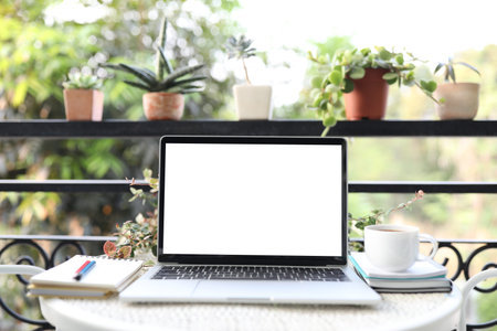 Laptop white mock up blank screen and notebooks and coffee cup on white table outdoorの写真素材