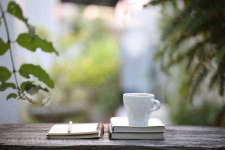 White coffee cup and notebooks with pencil on wooden table at outdoor
