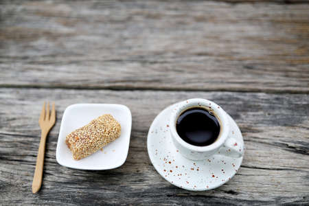 Coffee in white cup and peanut sesame bar snack and wooden folk on wooden tableの写真素材