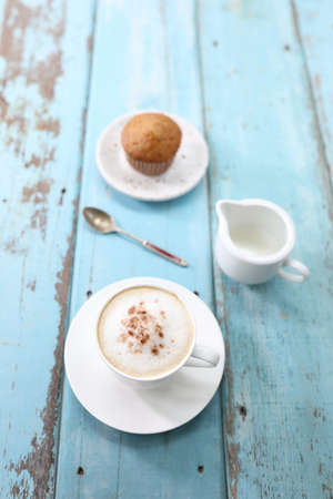 Cappuccino coffee cup and cupcake milk pitcher on blue wooden tableの写真素材
