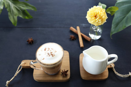 Latte coffee in glass cup and milk pitcher with rose flower on dark tableの写真素材