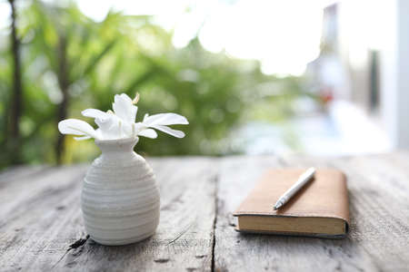 Butterfly lily flower and leather notebook with pen on wooden tableの写真素材