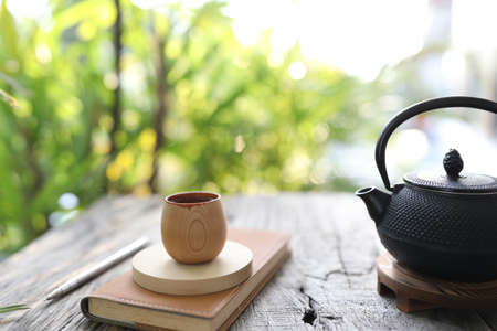 Metal teapot and bamboo cup with brown notebook on wooden tableの写真素材