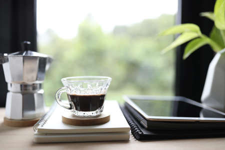 coffee glass cup and notebooks and tablet with moka pot in front of windowの写真素材