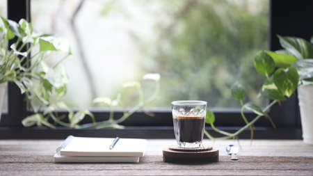 Diary notebook and coffee cup in on wooden table with window viewの写真素材