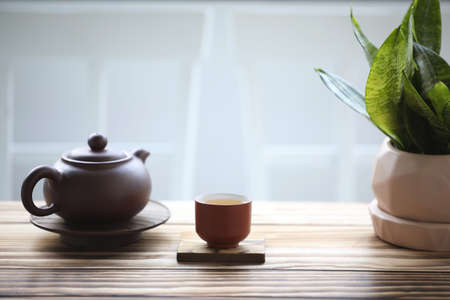 pottery teapot and tea cup and snake plant on brown wooden tableの写真素材