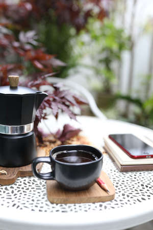 Black coffee cup and moka pot with phone and notebook on blue wooden table