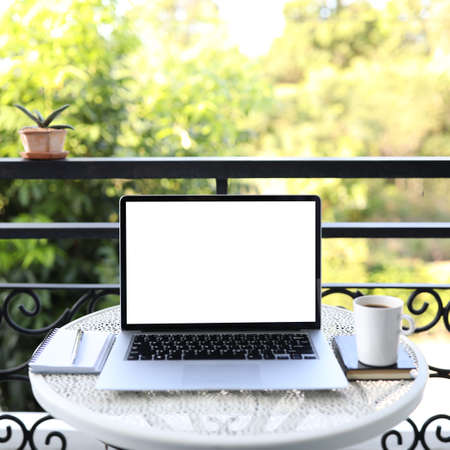 Laptop side view and coffee cup with notebooks on white table outdoor