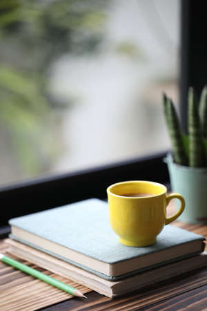 Notebook and yellow cup on and plant pot wooden table in fornt of windowの写真素材