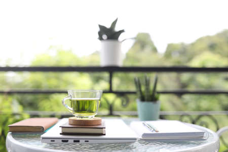 Green tea glass cup and folded laptop and notebooks on glass table balcony outdoorの写真素材