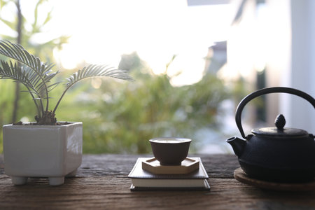 Metal tea pot and tea cup and plant pot on wooden table balcony outdoorの写真素材