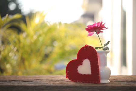Red rose in a white vase and heart fabric on wooden tableの写真素材