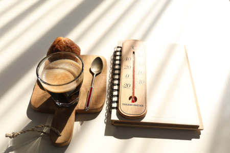 Flat lay Coffee and cup cake and notebook and thermometer with sunshineの写真素材