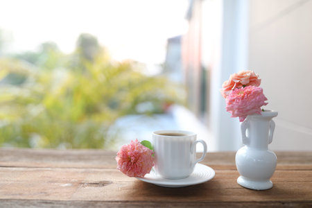 ceramic coffee cup and a white vase of rose flowersの写真素材