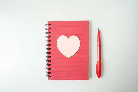 red notebook with heart and red pen on white table