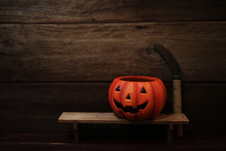 Dark Halloween pumpkin with old rustic scythe on wooden table and wallの写真素材