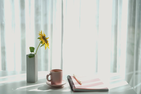 Coffee in a pink cup and pink notebook and pen with sunflower on white table minimalist interiorの写真素材