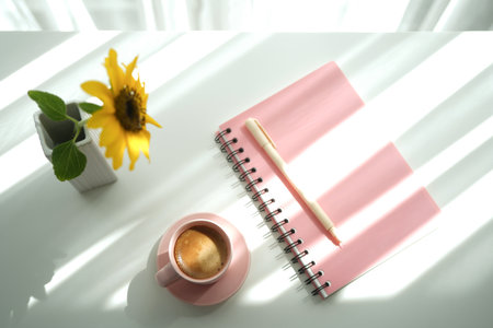 Pink cup and notebook with sunflower on white tableの写真素材