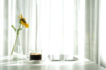 Coffee in a glass cup and tablet with sunflower on white table minimalist interiorの写真素材