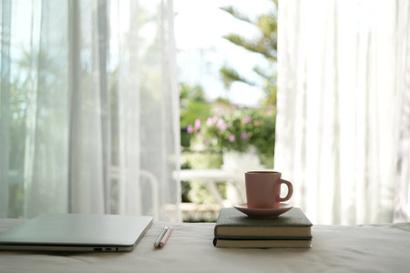Coffee cup and notebooks on bed with windows viewの写真素材
