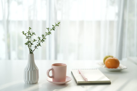 Tall plant vase and pink cup with notebook by the window, minimal interior, cozy workspaceの写真素材