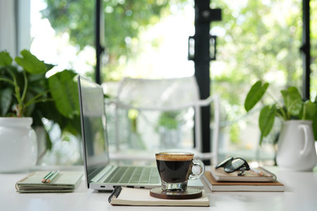 Laptop side view and coffee glass cup and notebook, cozy indoor workspaceの写真素材