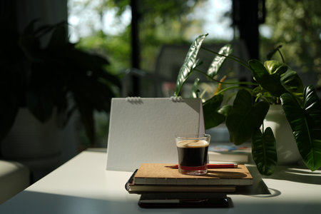 Coffee glass cup and notebook on white table under morning sunlightの写真素材