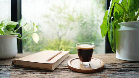 Coffee and brown notebook on rustic wood table by the windowの写真素材