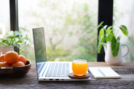 Side view of a laptop with fresh orange juice on rustic wooden table, by the windowの写真素材