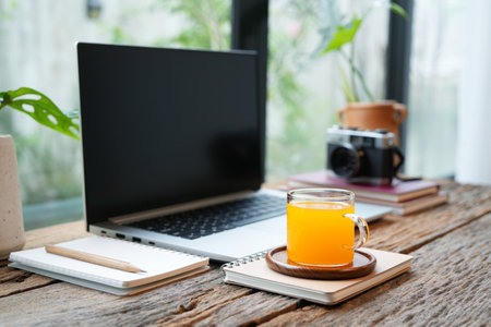 Orange juice and a laptop and notebook, cozy workspace by the windowの写真素材