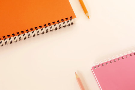 Orange and pink color pencil and spiral notebook on a white deskの写真素材