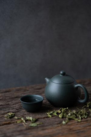 Dried tea in dark blue earthenware tea set on a rustic wooden table, with dark grunge wall in a...