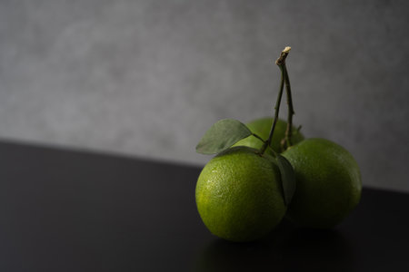 Unripe Citrus sinensis fruit, a natural hybrid between pomelo and mandarin, displayed on a black surface with a dark grunge backgroundの写真素材