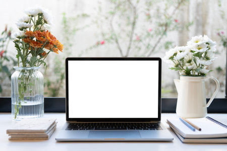 Laptop and notebook with flowers vase on white desk by the windowの写真素材