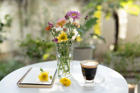 Flowers and coffee and notebook on a white table, serene garden