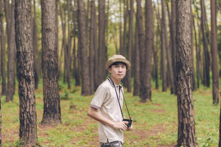 Asia man wears shirt, hat, and camouflage pants are walking and taking photos at the forest.の写真素材